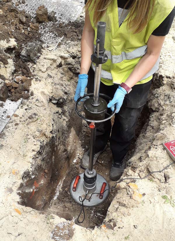 Engineer in a high-visibility vest carrying out a plate load test in an excavation trench